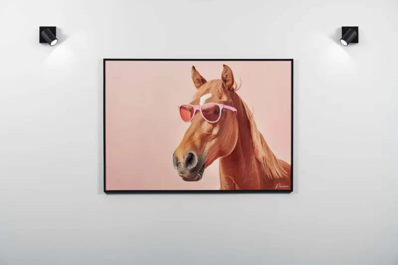 Un tableau encadré représentant un cheval brun portant des lunettes de soleil roses sur un fond rose doux.