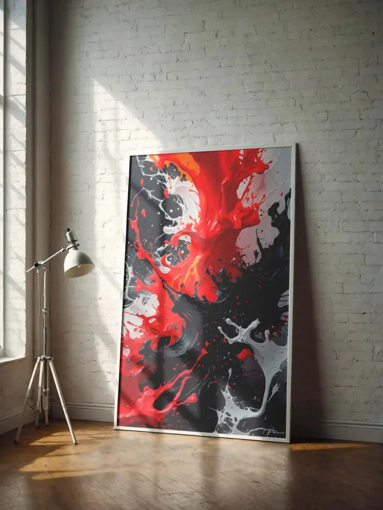 Une peinture abstraite audacieuse avec des éclaboussures vives de rouge, noir et blanc dans un cadre moderne est appuyée contre un mur de briques blanches.