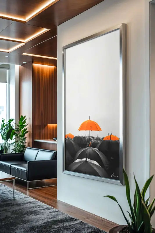 Une œuvre d’art moderne encadrée d’argent mettant en scène un parapluie orange frappant sur un fond de parapluies noirs, exposée dans un cadre de bureau élégant.