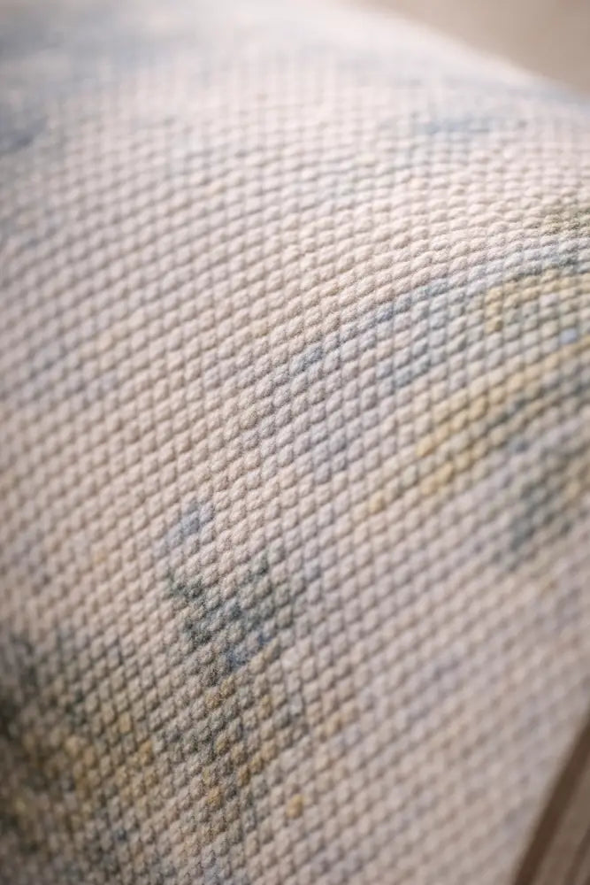 Un tissu tissé doux, blanc cassé, avec un motif texturé subtil et de légers accents floraux bleu-gris.
