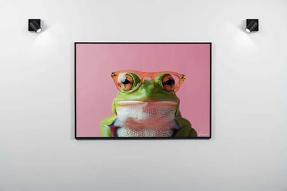 Une photographie encadrée d’une grenouille verte portant des lunettes à monture orange sur un fond rose.