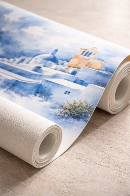 Un rouleau de papier peint présentant une représentation à l’aquarelle de bâtiments blanchis à la chaux et de toits bleus sous un ciel doux.