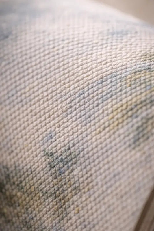 Un tissu tissé doux, blanc cassé, avec un motif texturé subtil et de légers accents floraux bleu-gris.