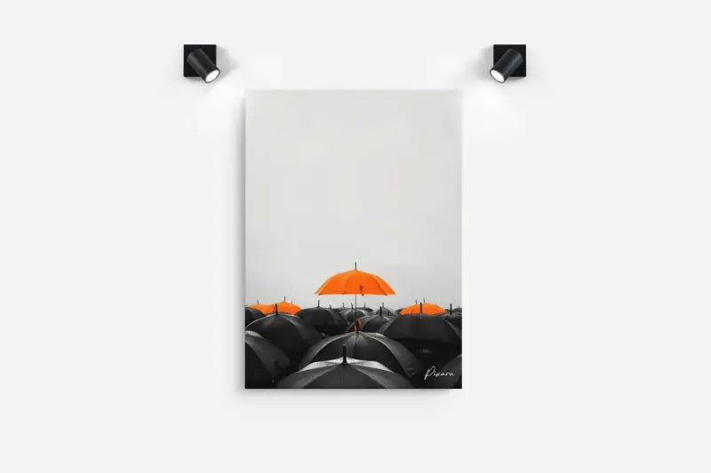 Une impression sur toile minimaliste mettant en vedette un seul parapluie orange vibrant se distinguant contre une mer de parapluies noirs, encadré par deux projecteurs encastrés élégants montés au mur.