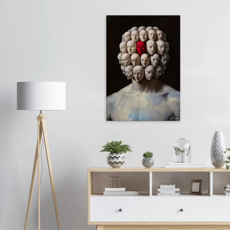 Un impressionnant tirage sur toile présentant une sculpture surréaliste de multiples têtes humaines disposées en motif circulaire autour d’une figure centrale, avec une tête mise en évidence en rouge vif par contraste avec les tons atténués des autres.